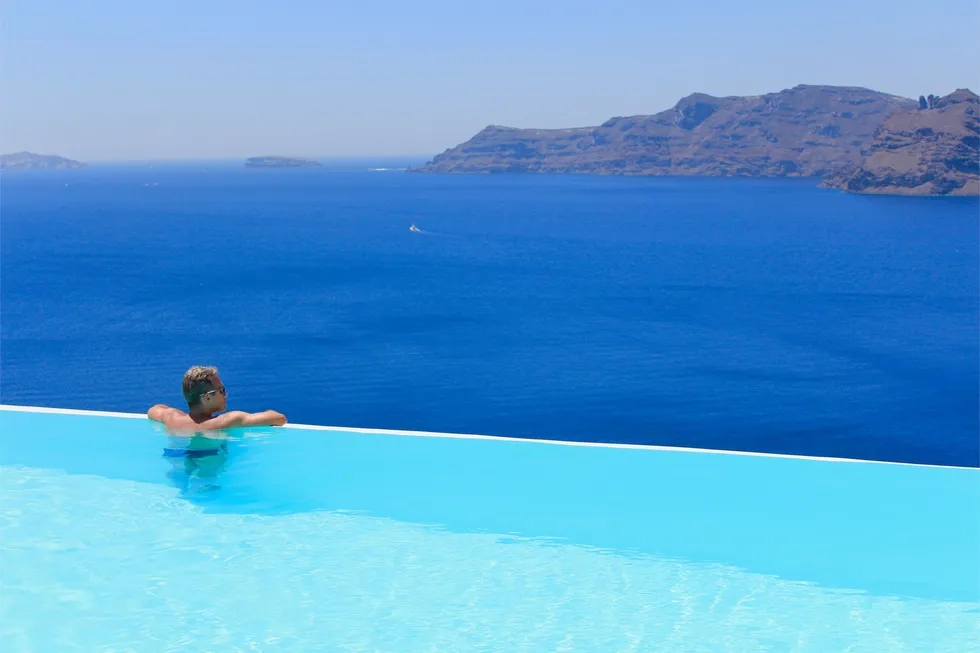 man in blue infinity pool over bay in Oia, Santorini, Greece