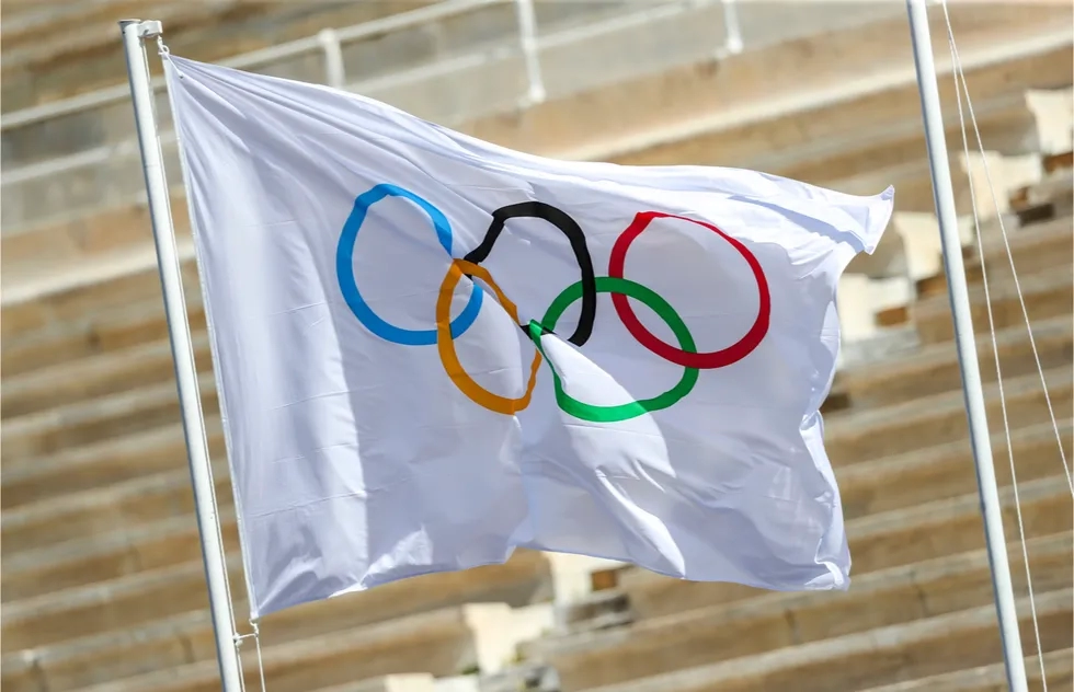 Olympic flag flying in front of empty stadium stands