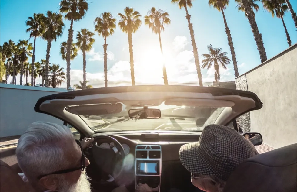 senior couple in rental car driving toward palm trees