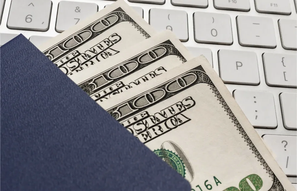 $100 bills on computer keyboard inside blue passport-like cover