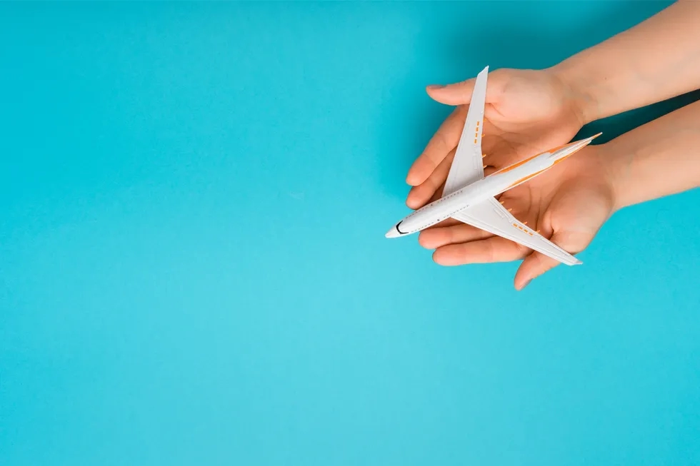 hands cradling model airplane over plain blue background