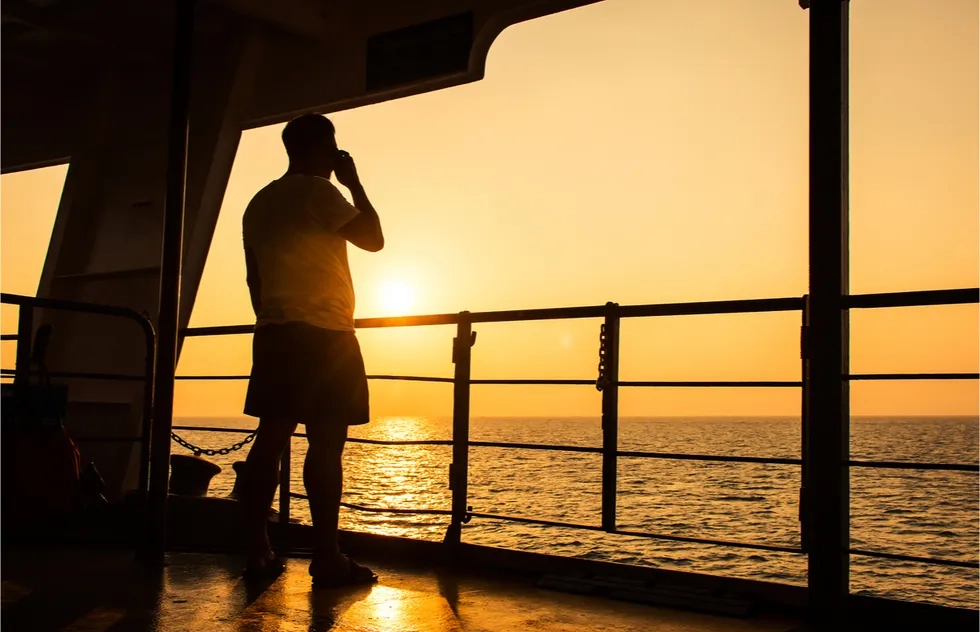 man on cruise deck using cell phone in sunset