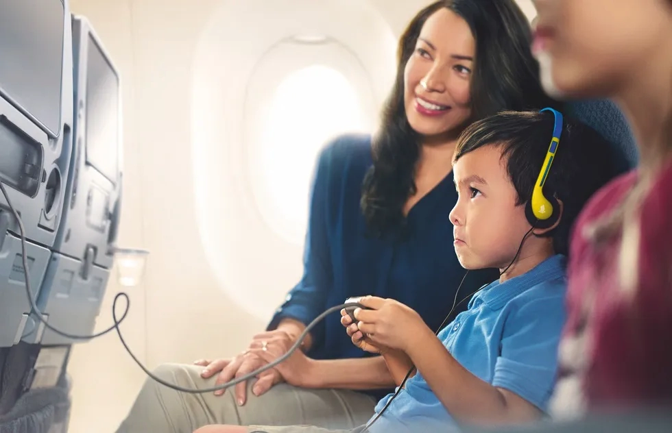 Child playing seatback game on airplane as mom watches