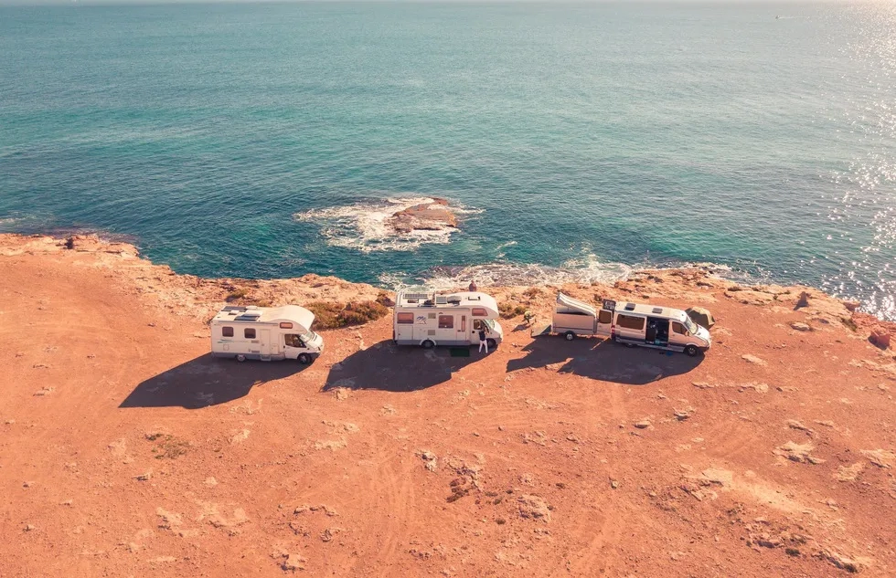 three RVs parked on orange coast by blue water