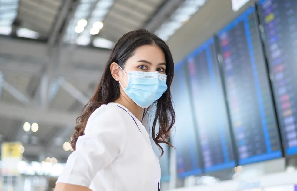 woman wearing mask in airport by departures board