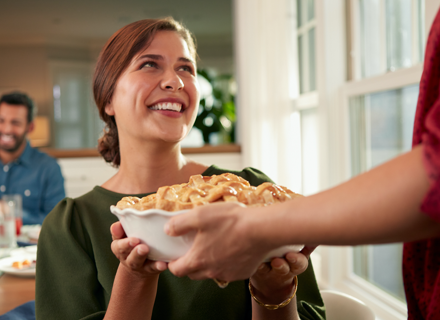 Woman smiling welcomingly at guest handing her a fresh pie for a dinner party