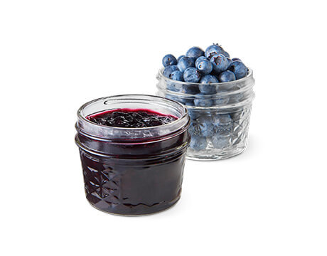 A jar of fresh blueberry jam in front of a jar of fresh blueberries