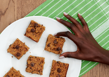closeup of a hand reaching to grab a chickpea blondie bar from a plate