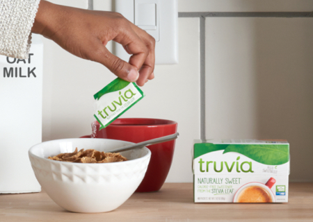 hand holding a Truvia packet and sprinkling its contents on a bowl of cereal