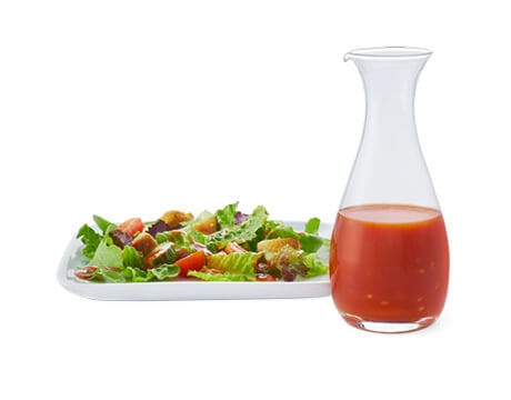 French Dressing in a clear carafe next to a plate of salad