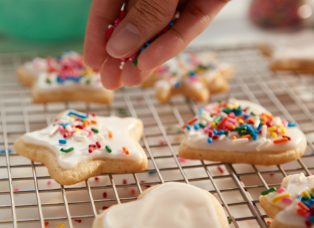 Closeup of hand sprinkling candy sprinkles on freshly frosted sugar cookies on cooling rack