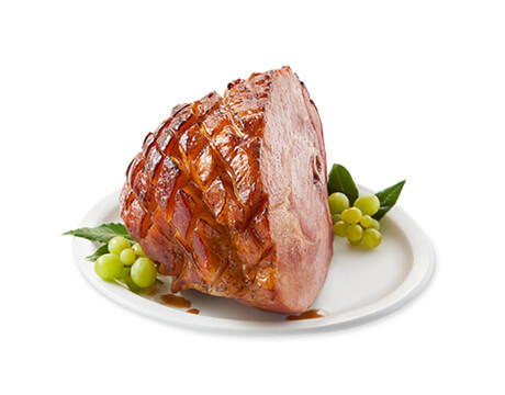 Unsliced glazed ham on a plate with green garnish