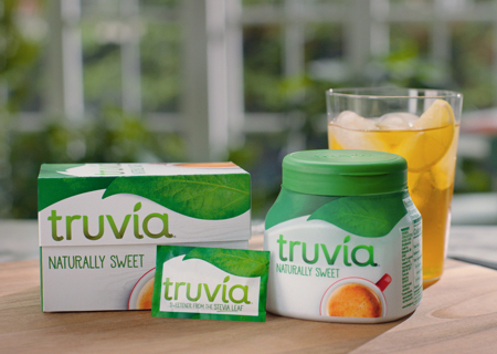 Truvia packets and spoonable jar posed next to a glass of lemonade