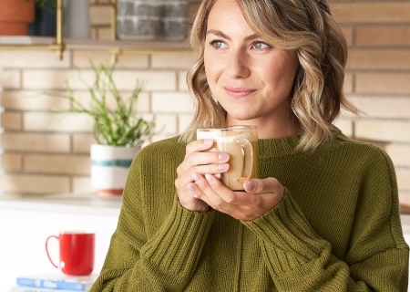 Woman holding a latte with both hands and smiling