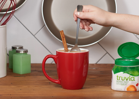 Mixing a spoonful of Truvia natural sweetener into a chai latte with a cinnamon stick