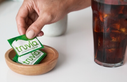 Truvia packets in wooden dish next to glass of iced tea