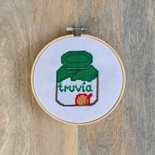 Framed cross stitch of Truvia spoonable on wood table surface