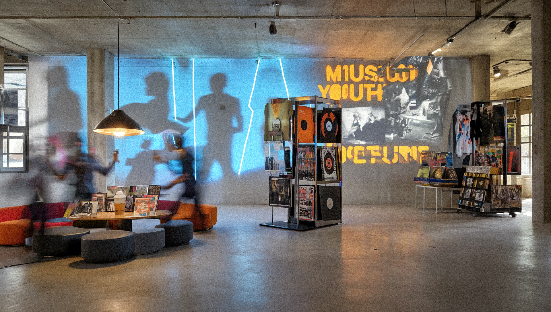 Museum exhibition space with blue projected silhouettes on wall, orange "MUSIC ON" and "OFFLINE" text, vinyl record displays, visitors walking through polished concrete floors.