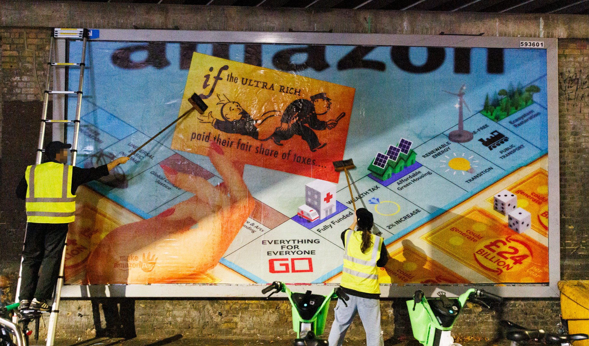 Workers in high-vis vests painting large mural on brick wall showing colourful board game layout with orange, blue, green and yellow squares.