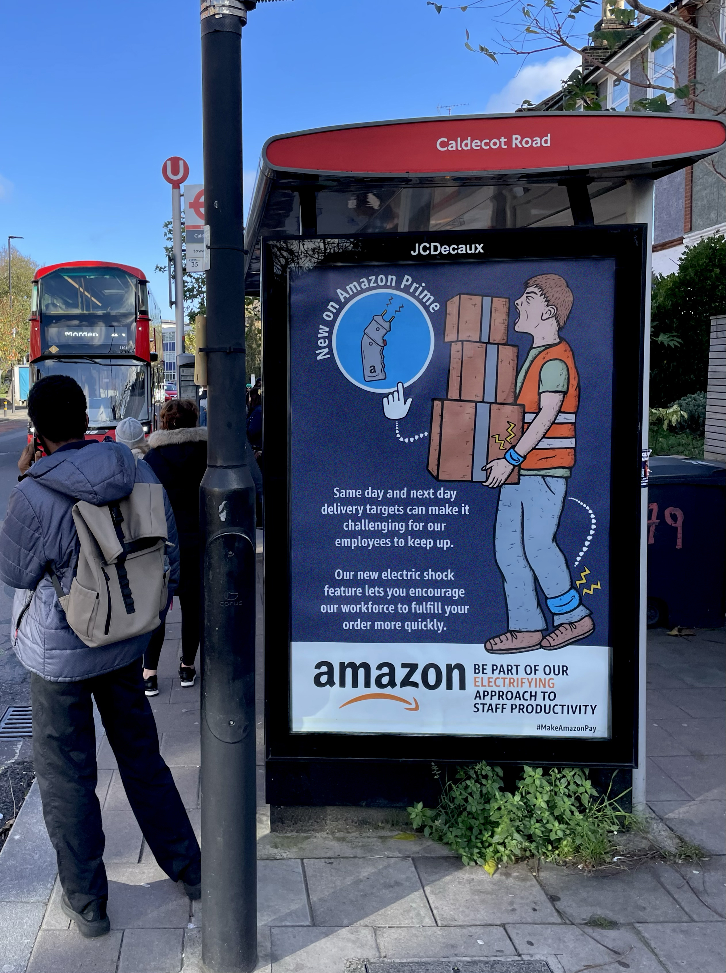 Amazon recruitment advert at Caldecot Road bus stop showing cartoon delivery worker with electric shock feature and productivity messaging.
