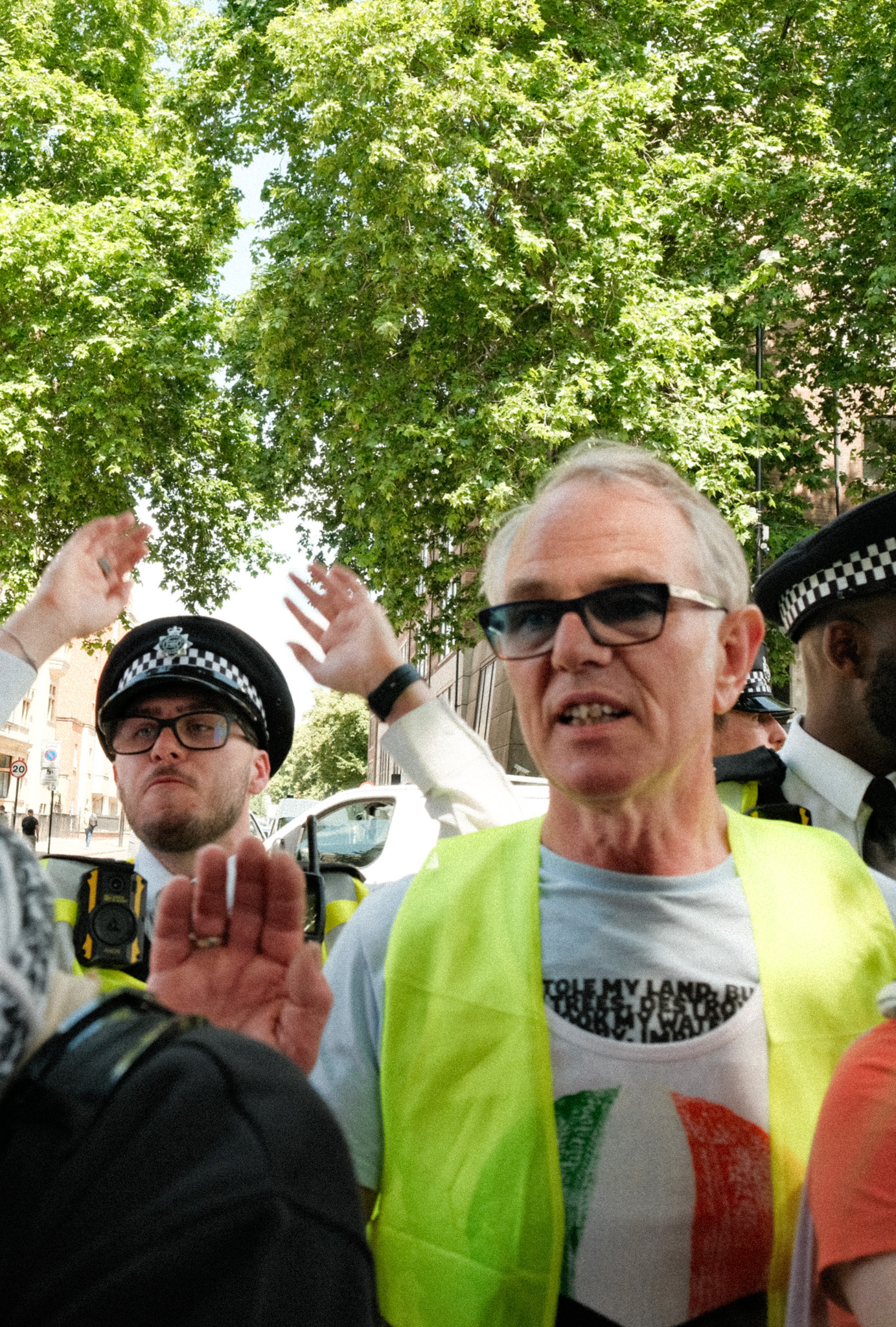 Two police officers wearing high-visibility jackets, one of whom is an older man with grey hair and glasses.