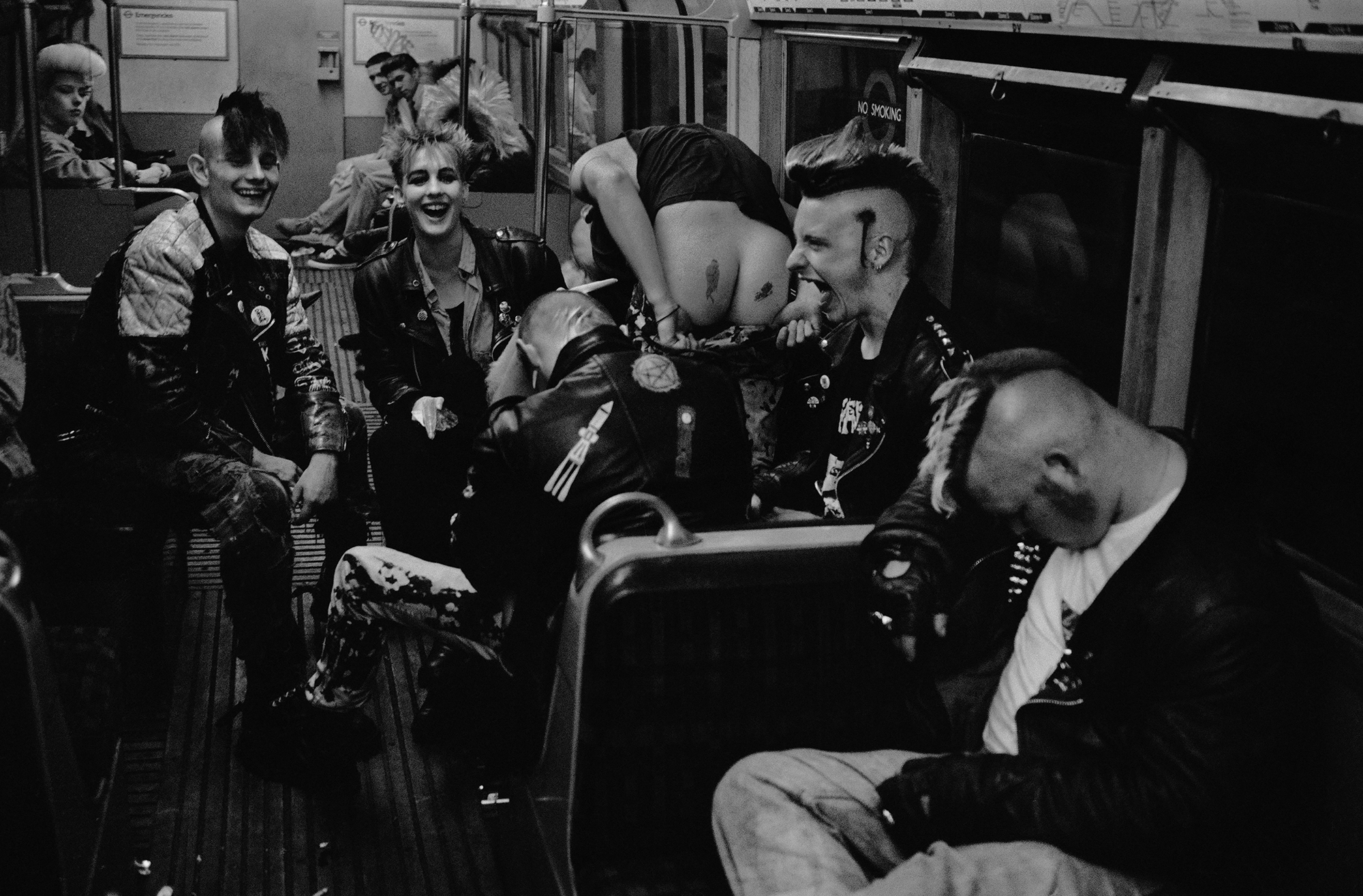 Group of punk rockers with mohawks and leather jackets gathered inside what appears to be a train carriage or bus, black and white image.
