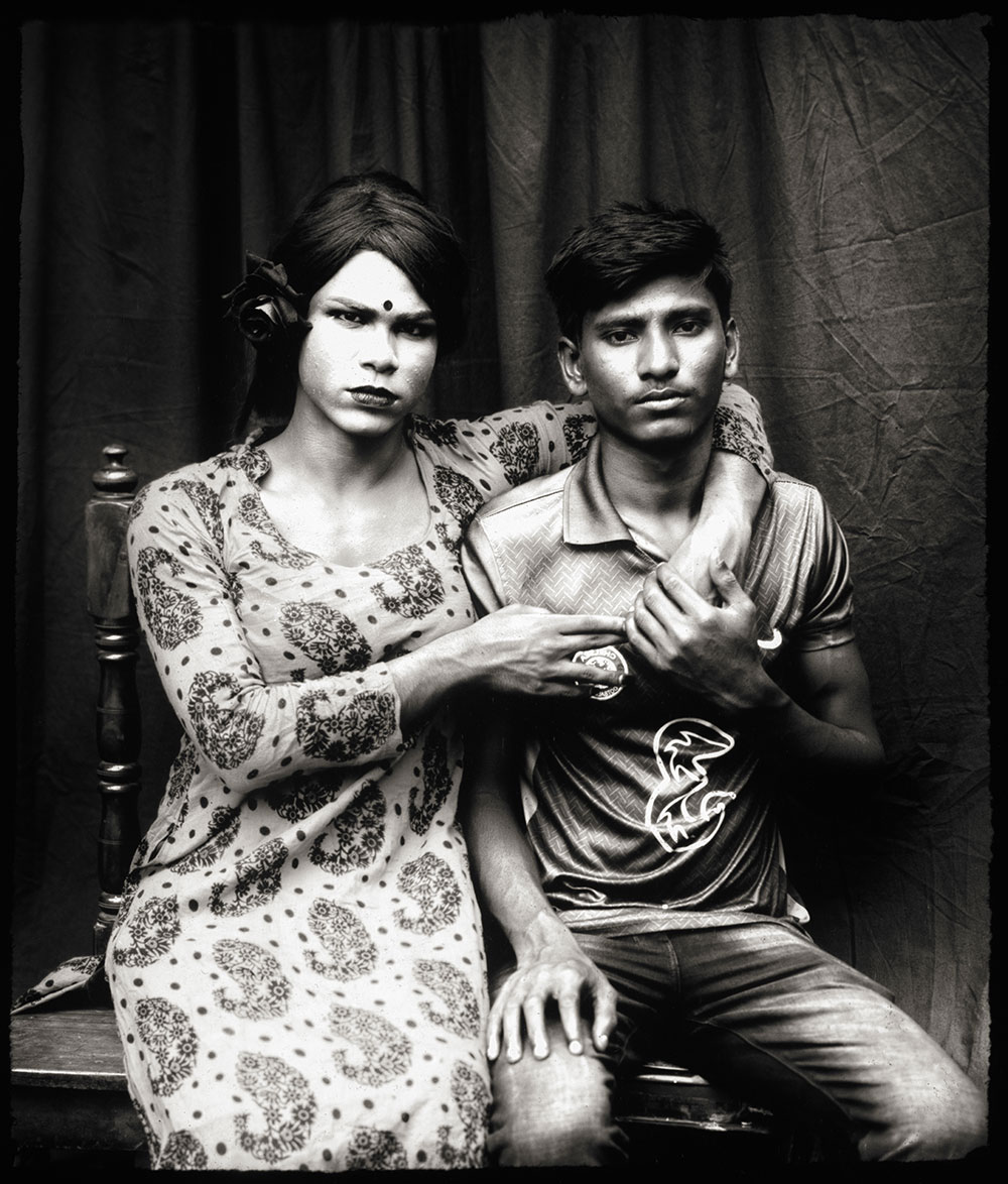 Woman in patterned sari with bindi and man in polo shirt sitting together on steps, desaturated tones with green-yellow lighting.