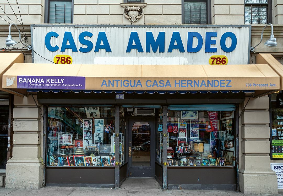 Storefront with large blue "CASA AMADEO" sign above shopfront displaying books and magazines in windows, cream stone building facade.
