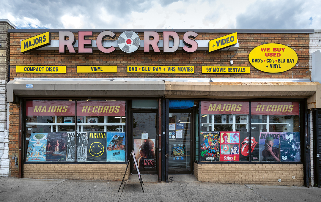 Record shop storefront with brown brick exterior, large "RECORDS" sign, yellow and red signage advertising CDs, vinyl, DVDs, and movie rentals.