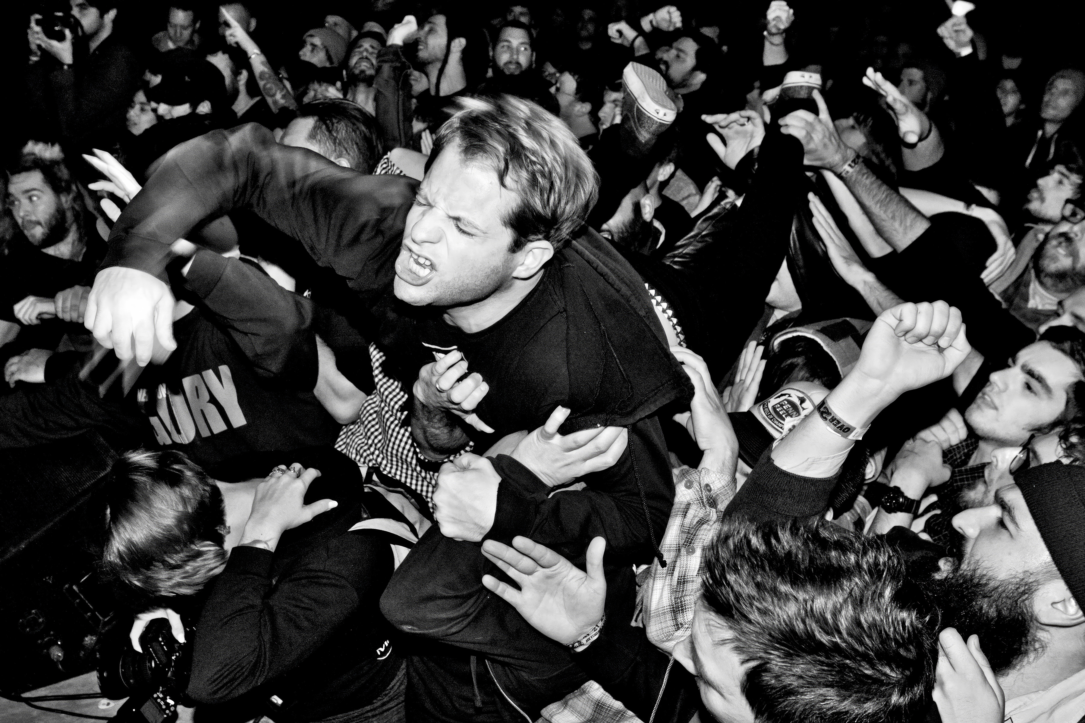 Black and white image of performer crowd-surfing at concert, supported by outstretched hands of densely packed audience below.