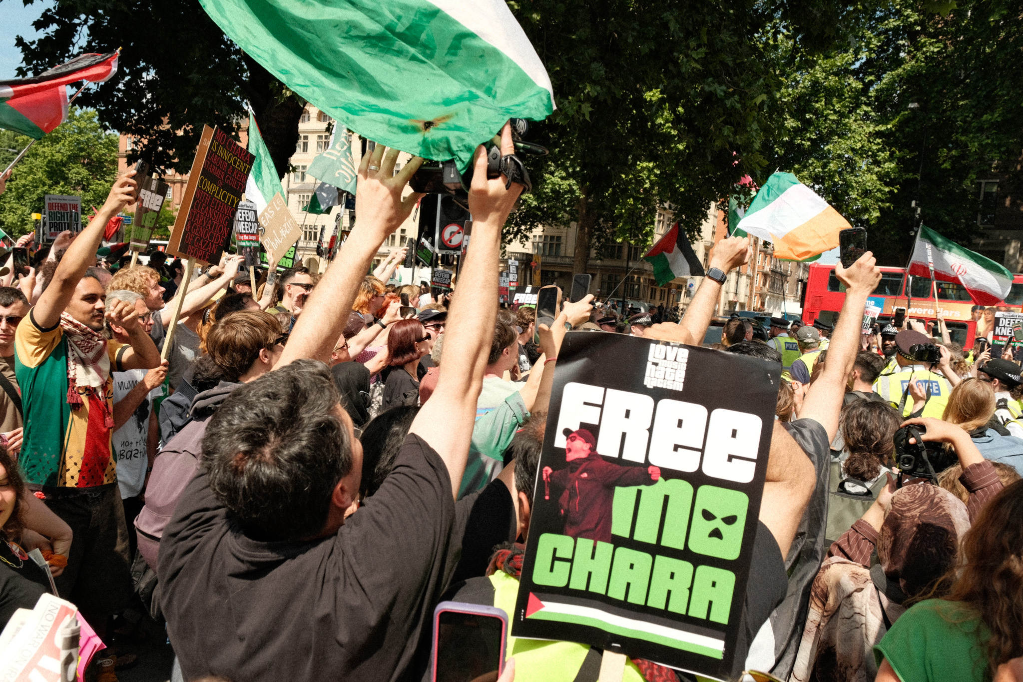 Crowd of people waving green flags and placards demanding "Free Maschar" at a protest