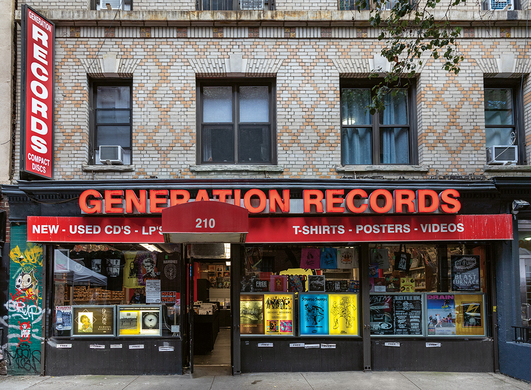 Generation Records storefront with red signage on beige brick building. Black shopfront displays vinyl records in windows, street number 210.