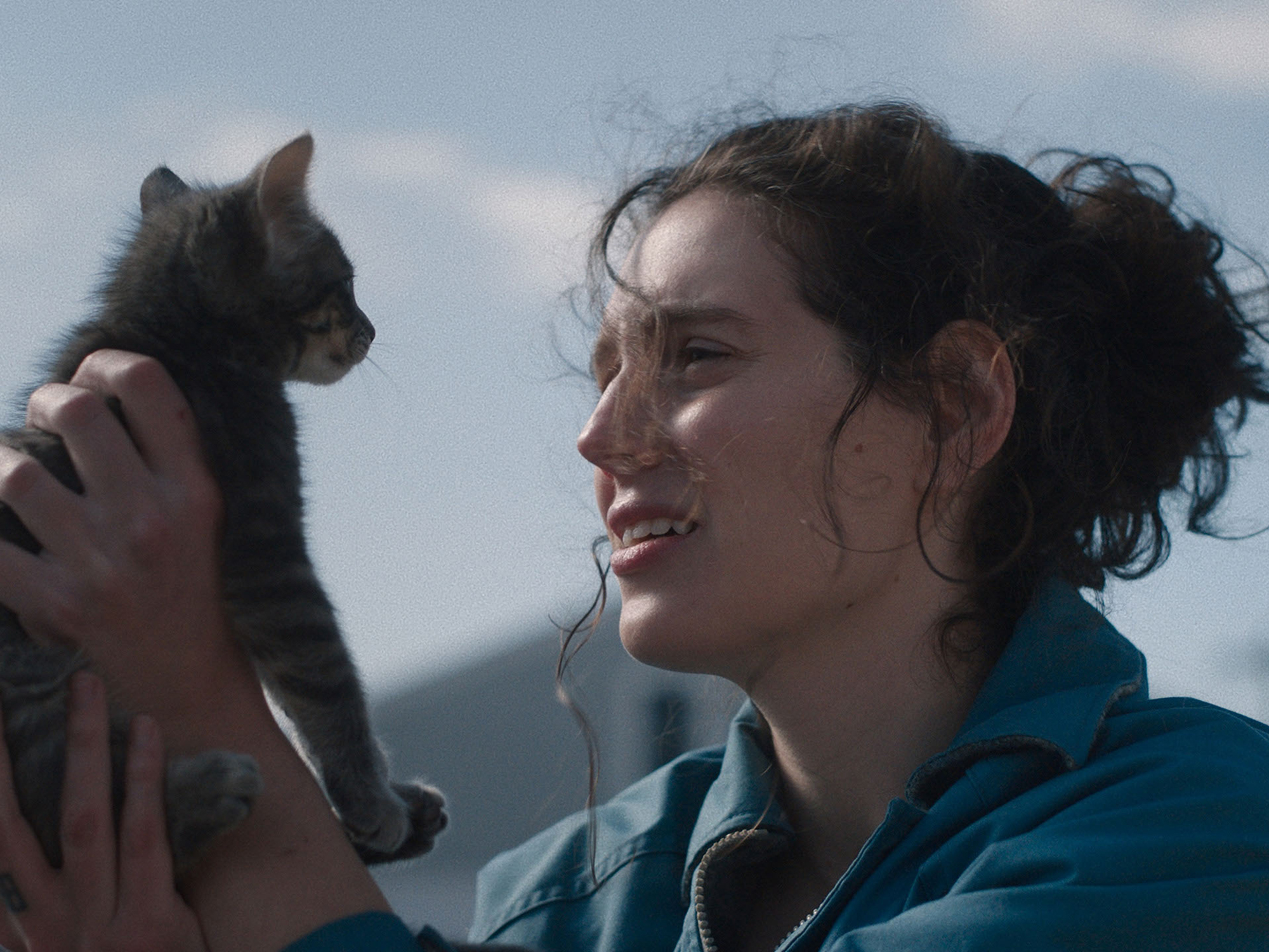 Close-up of a person gently cradling a black cat, both looking directly at the camera.