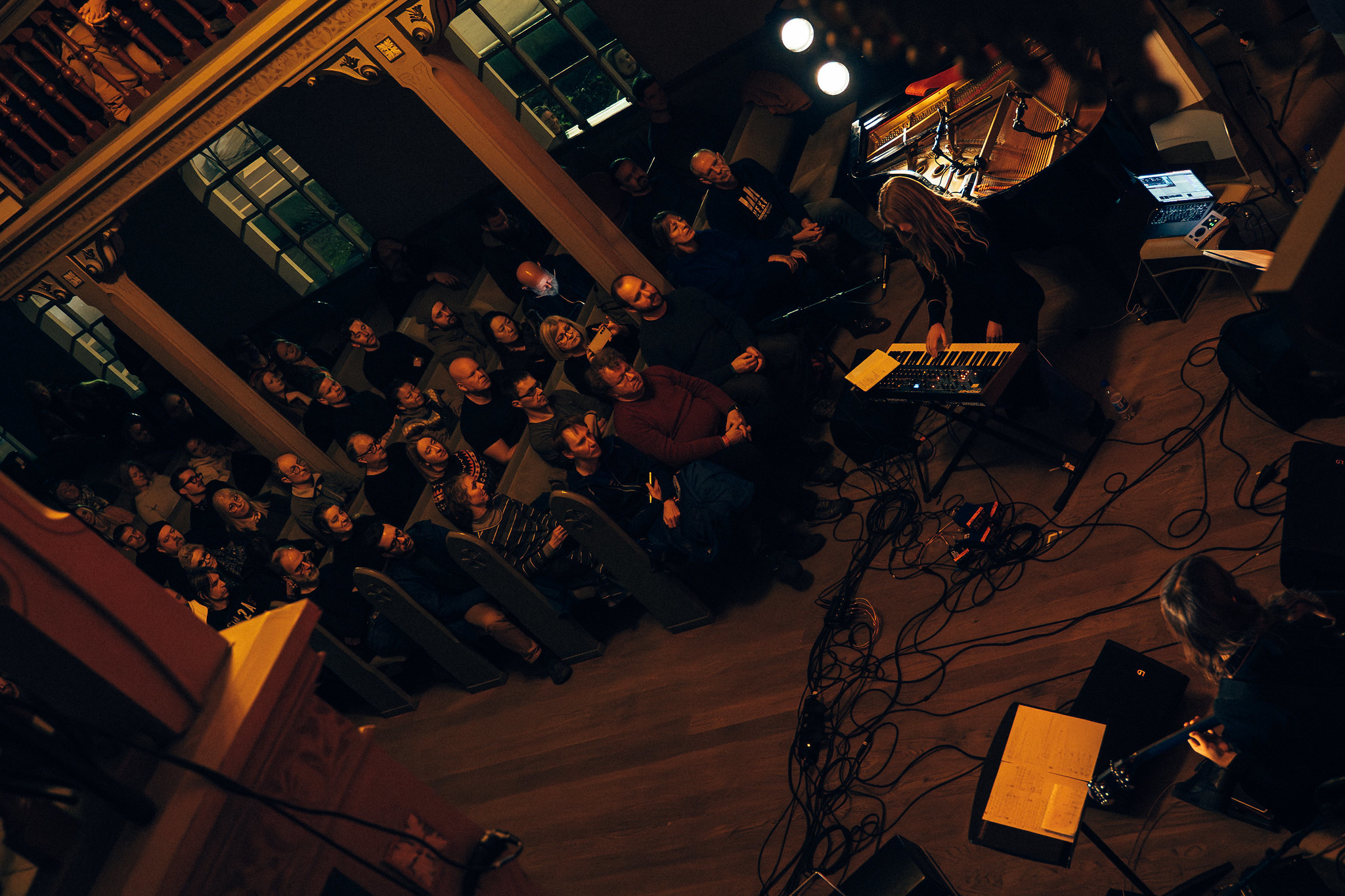 Overhead view of dimly lit venue with orange-lit seating area, dark performance space, and warm amber lighting throughout interior.