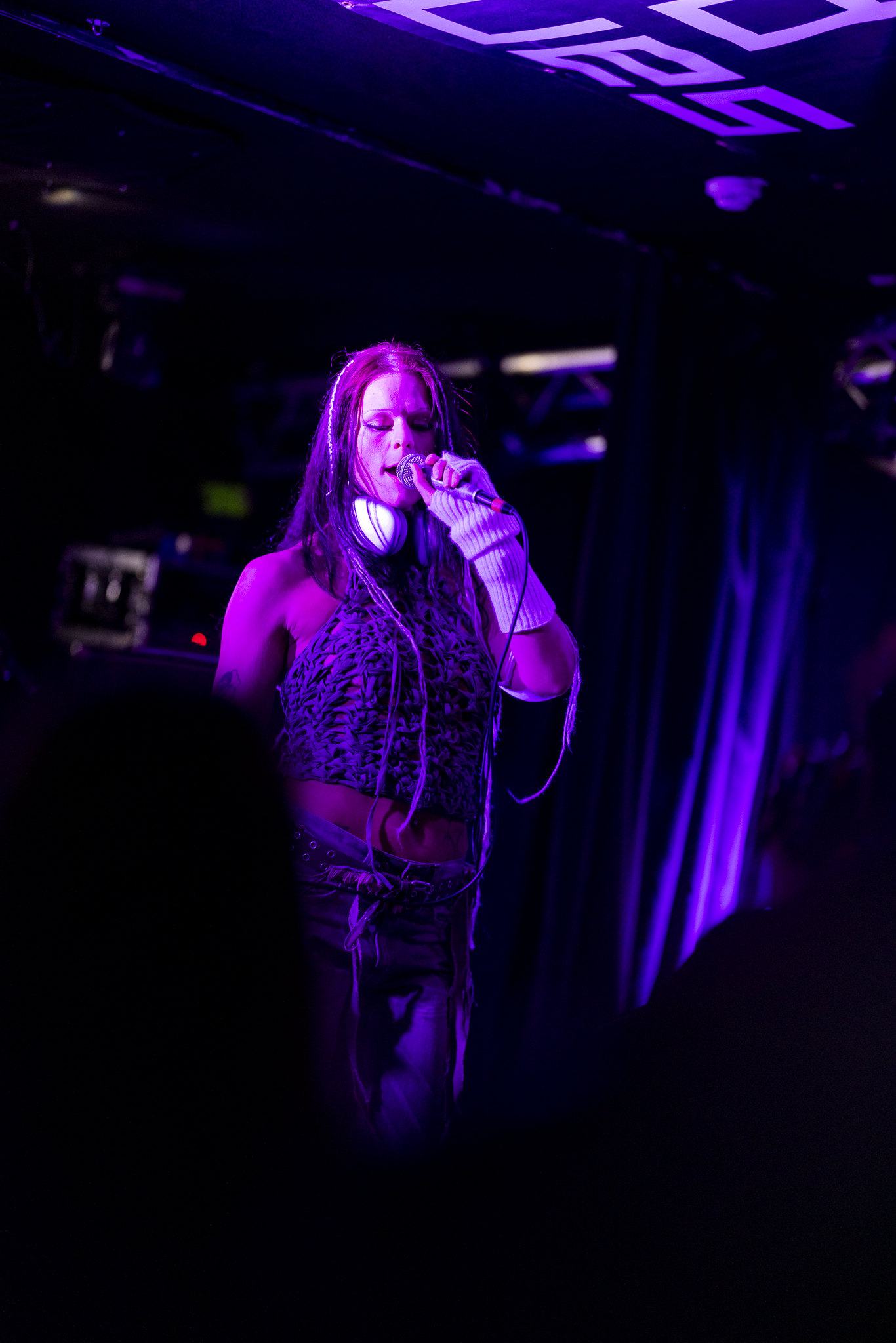 Woman singing into microphone on stage under purple and blue stage lighting in dark venue.