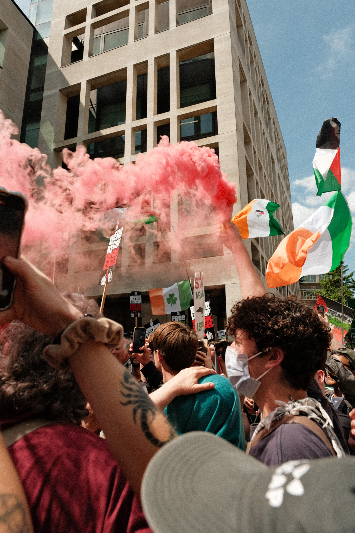 Protesters at rally; vibrant pink smoke, Irish flags, crowded city street
