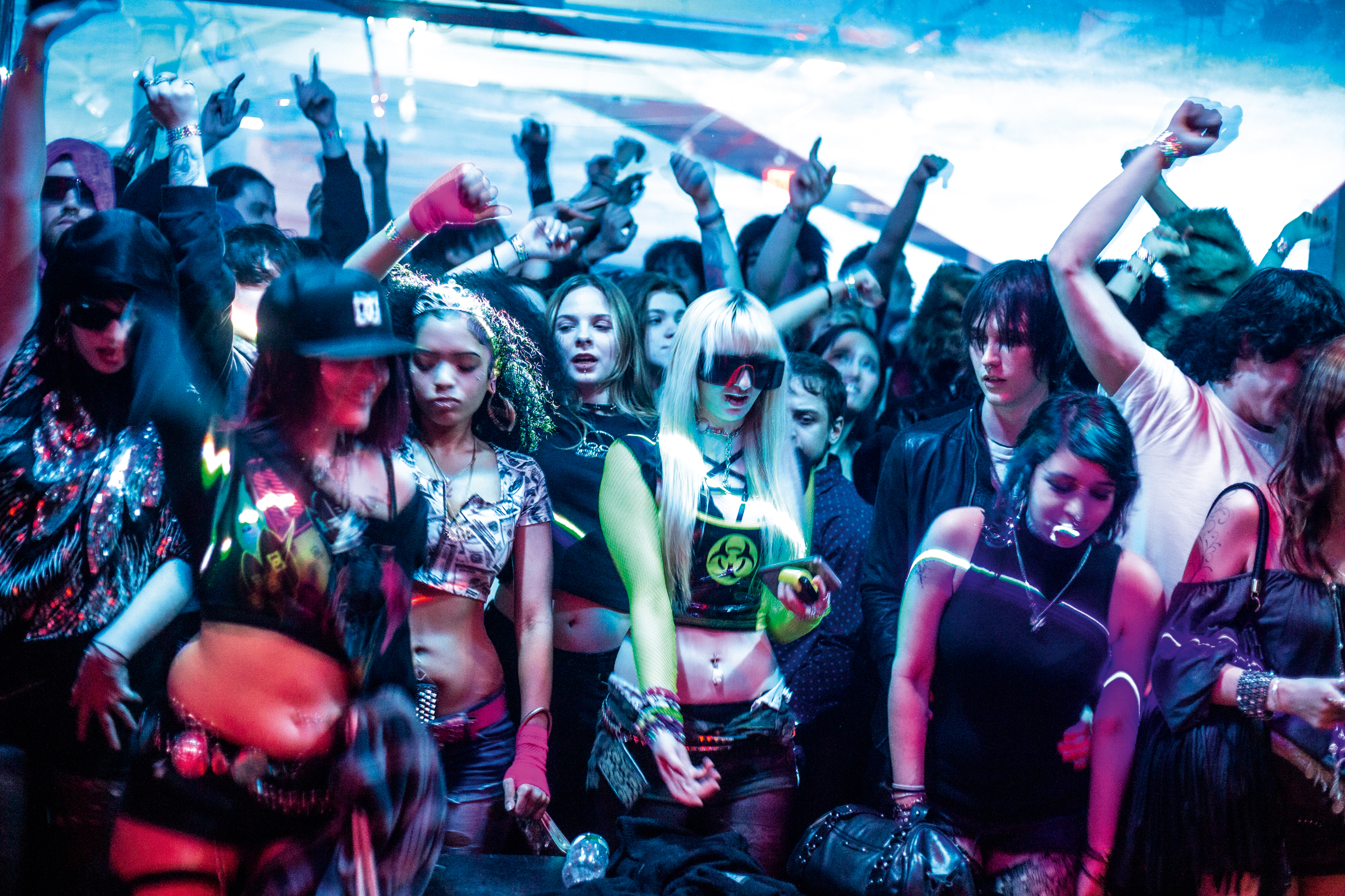 Crowd of people with raised arms in blue and red lighting, wearing dark clothing and accessories in nightclub setting.