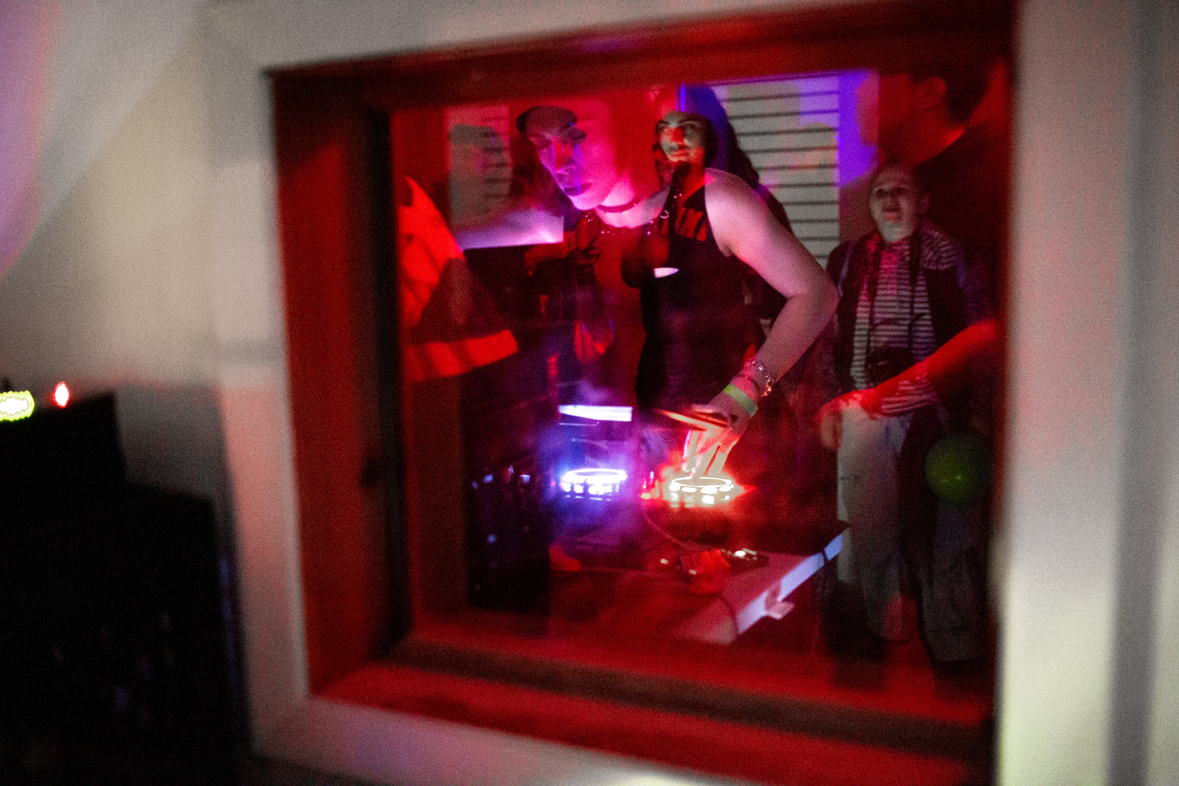 Red-lit display window with mannequins in dark clothing, purple and blue accent lighting, white wall frame.