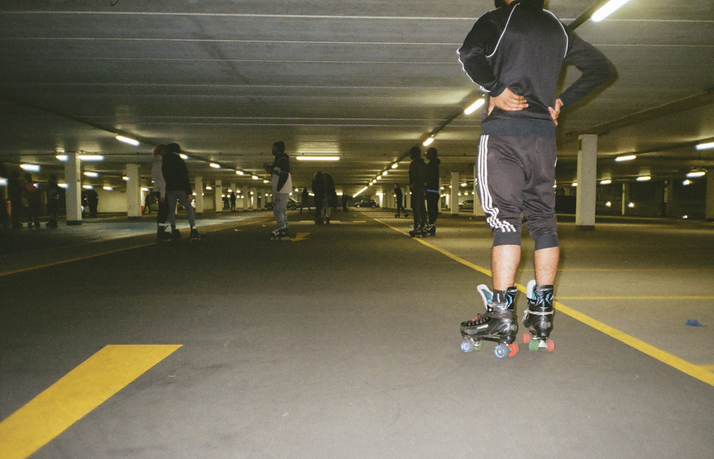 Person roller skating in underground car park with concrete floor, yellow lane markings, and fluorescent lighting overhead.