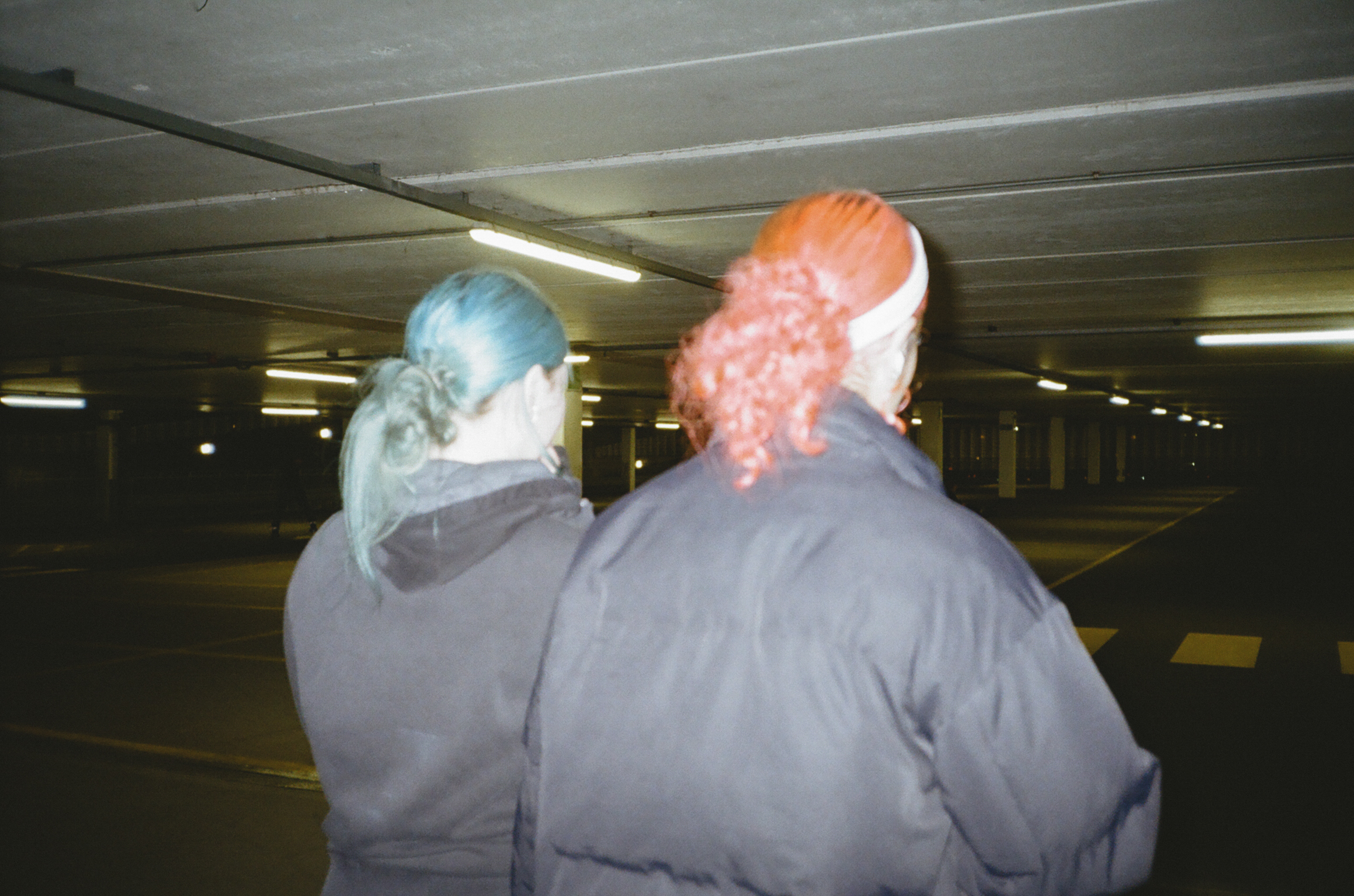 Two people wearing protective hairnets and grey clothing in industrial facility with fluorescent lighting and concrete ceiling.