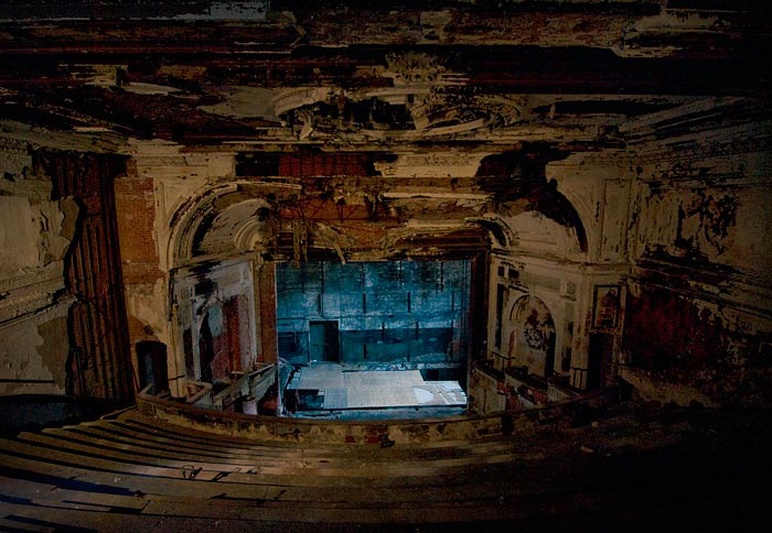 Ornate, dilapidated theatre stage with elaborate arched ceiling and balconies.