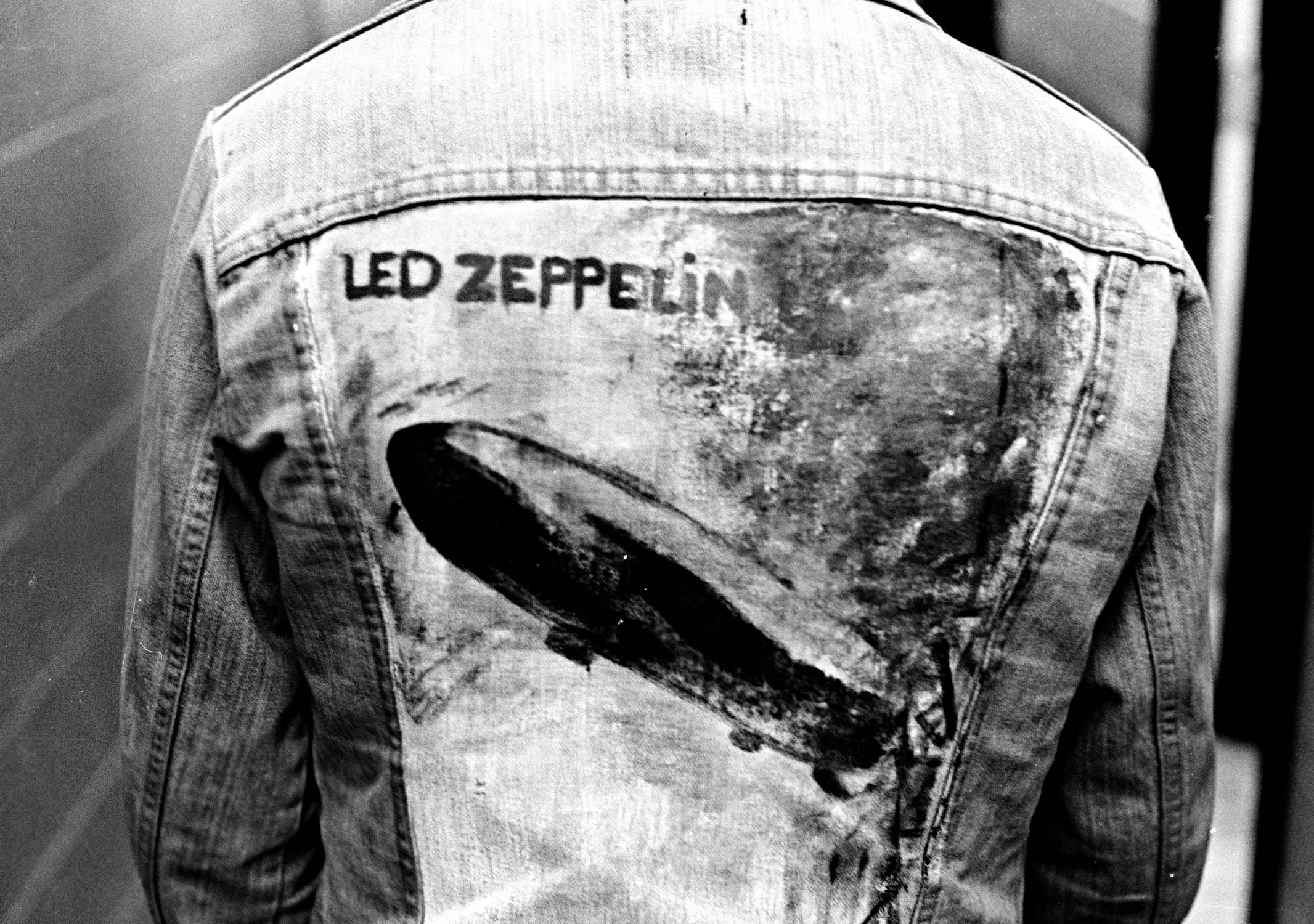 Black and white image showing the back of a denim jacket with "LED ZEPPELIN" text and airship graphic printed on it.