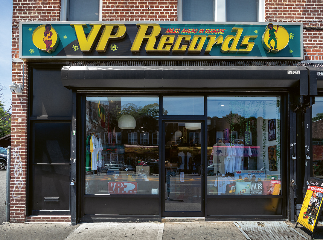 VP Records shopfront with yellow and green signage on red brick building, large windows displaying vinyl records and music merchandise.
