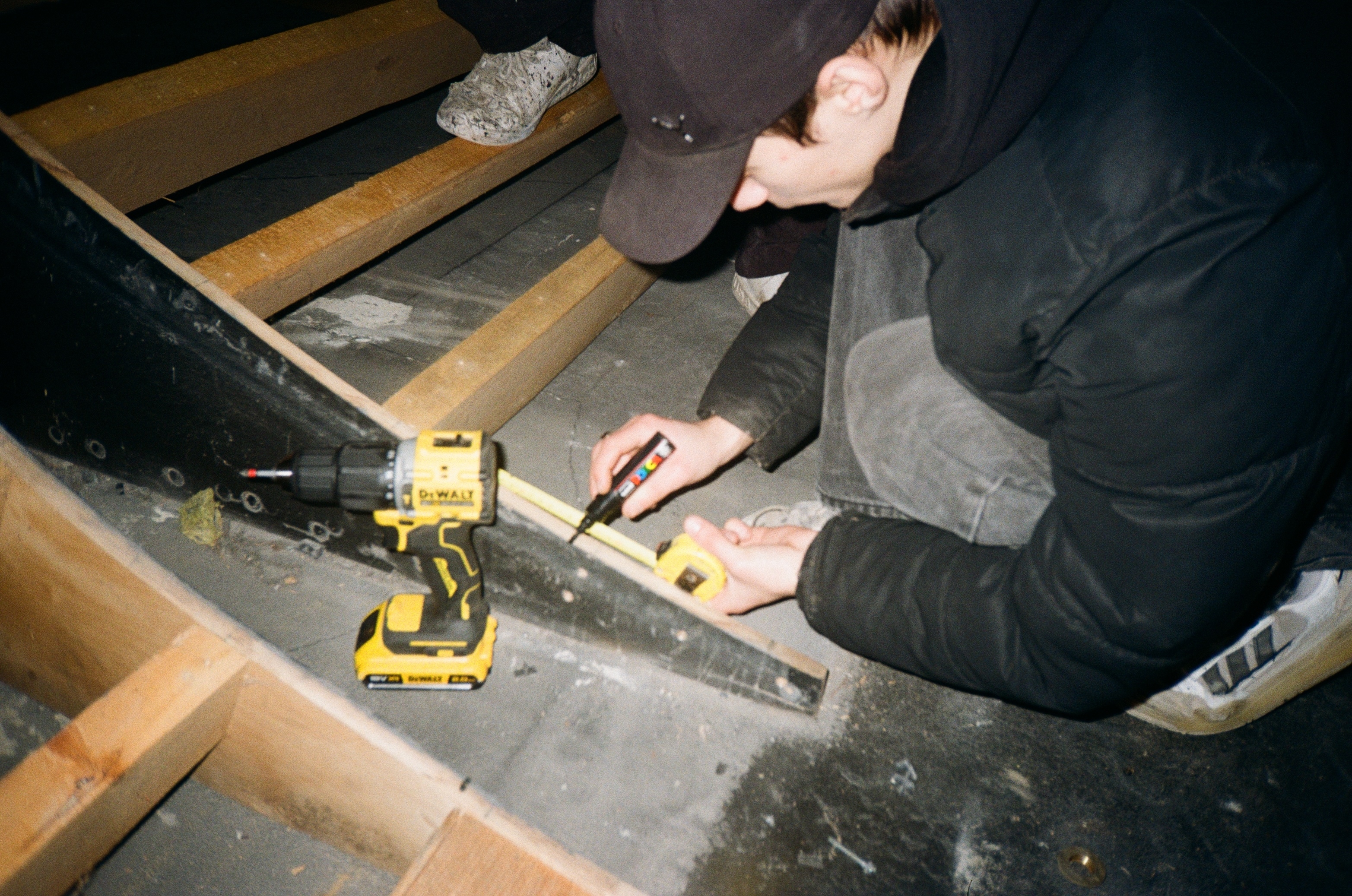 Person using power tools on wooden steps in dimly lit space.