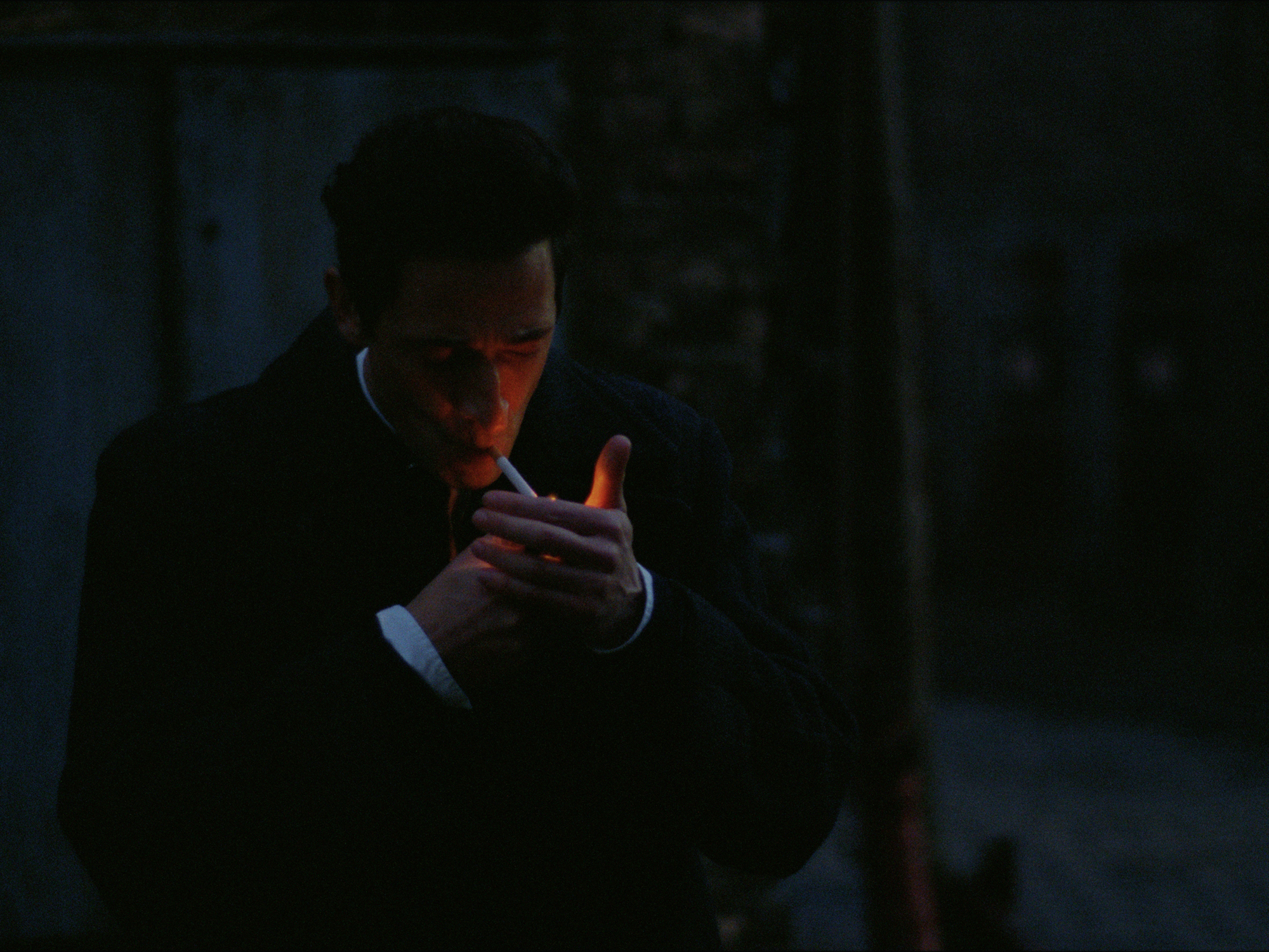 Silhouetted figure in dark suit using a mobile phone, against a shadowy background.