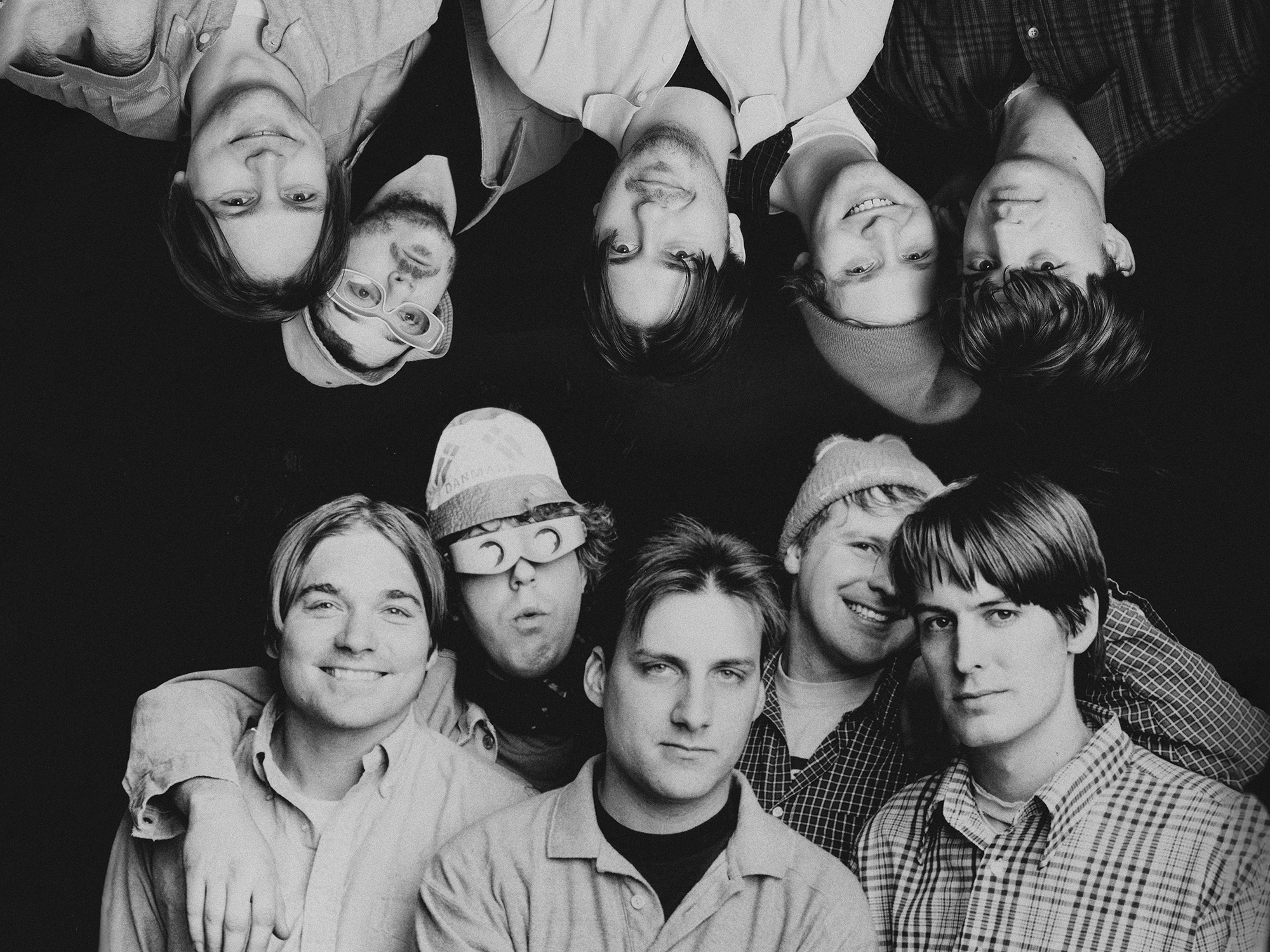 Group portrait of a band, with 10 individuals shown in black and white. The group is arranged in two rows, with members making various facial expressions.