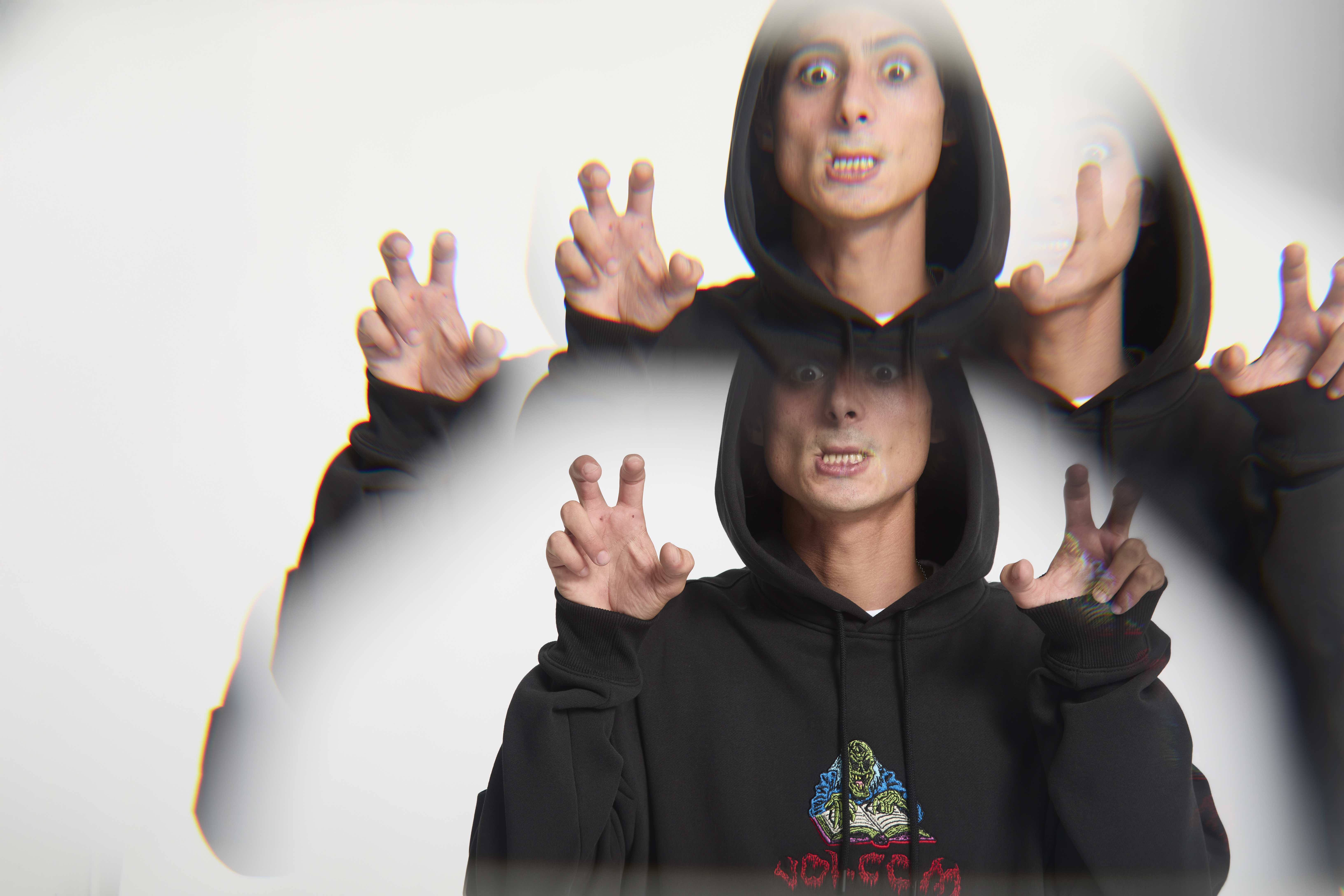 Two people in black hoodies with hands raised in claw-like gestures, making exaggerated facial expressions against white background.