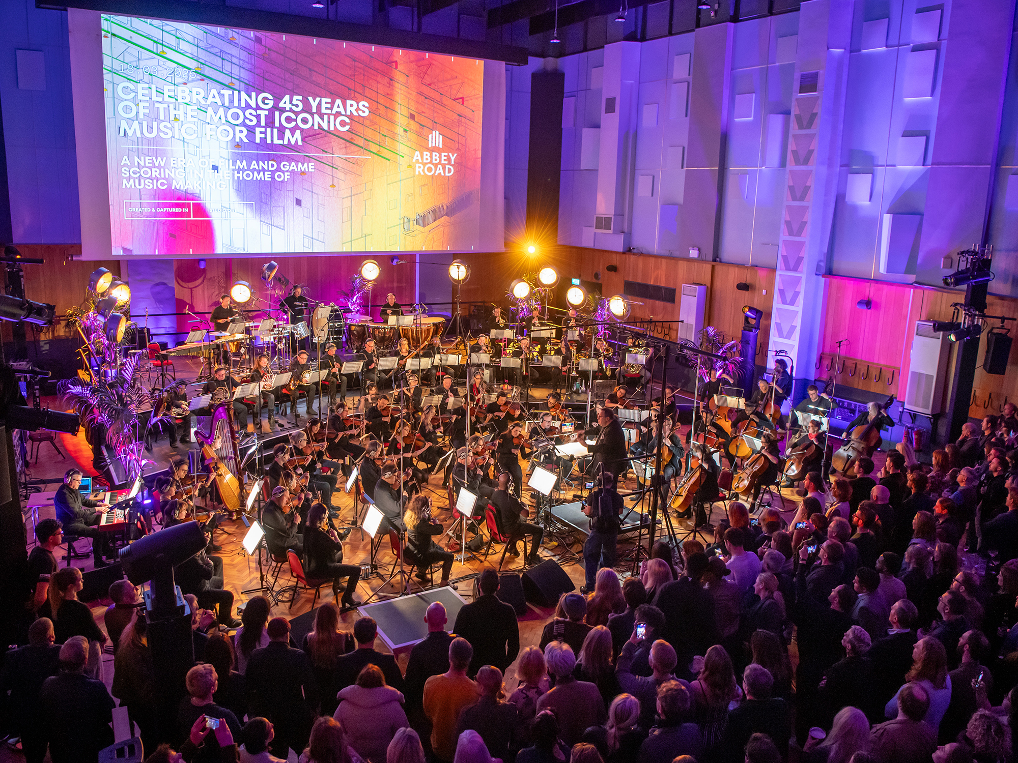 A large orchestra playing on stage at Abbey Road, with purple and blue lighting illuminating the performance.