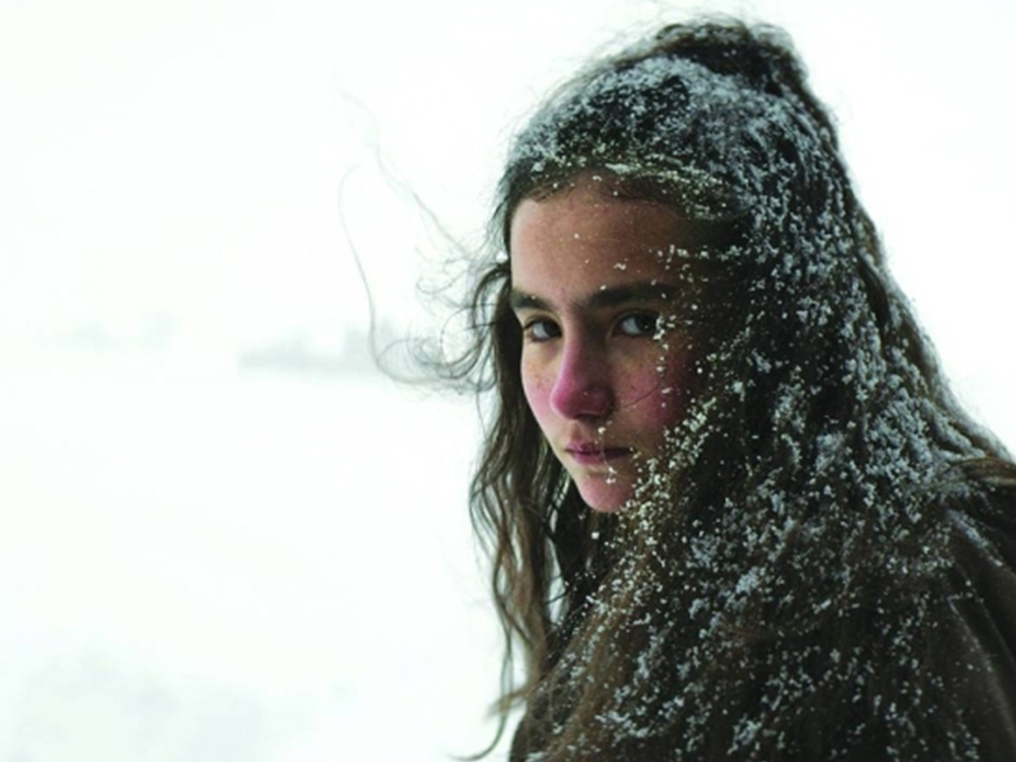 A person with long, dark hair partially covered in snow, with a serious expression on their face.