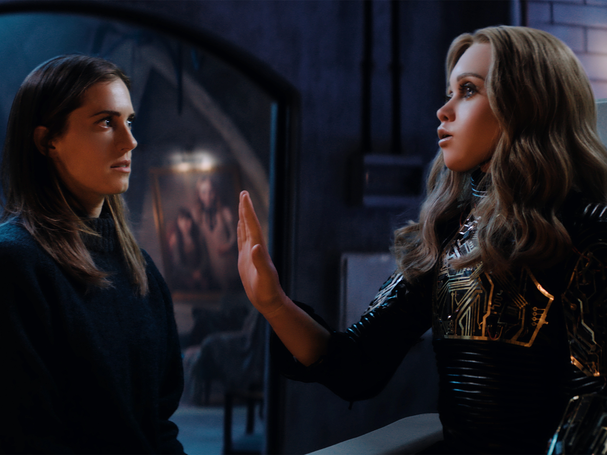 Allison Williams and M3gan engaged in conversation in a dark setting.